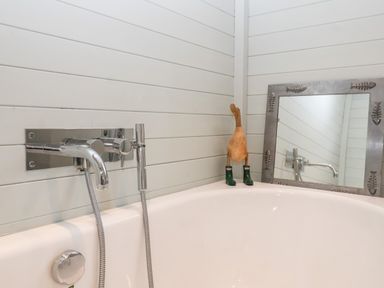 A bathtub with a wall-mounted faucet a wooden duck with green boots and a mirror with fish decorations at Lampland House in Walberswick