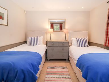 A bedroom with two single beds blue blankets striped pillows a gray dresser with lamps and a mirror at Lampland House in Walberswick