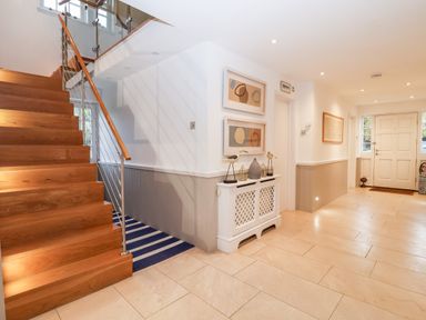 A hallway with wooden stairs a white radiator cover with decorative items and framed pictures on the wall at Lampland House in Walberswick