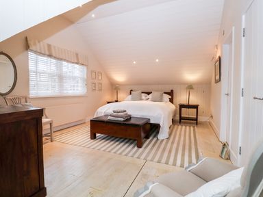A bedroom with a large bed bedside tables lamps and a striped rug at Lampland House in Walberswick