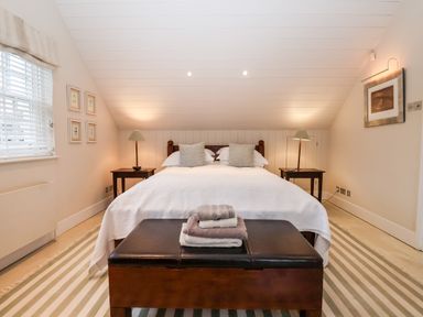 A bedroom with a double bed two bedside tables with lamps and towels on a bench at Lampland House in Walberswick