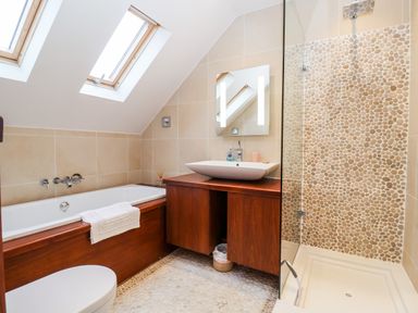 A bathroom with a bathtub under skylight windows a wooden vanity with a sink a mirror and a pebble tiled shower at Lampland House in Walberswick