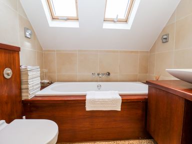 A bathroom with a bathtub under two skylights next to a wooden cabinet and a toilet at Lampland House in Walberswick