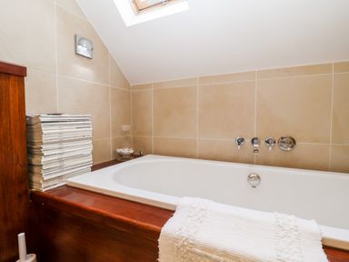 A bathroom with a bathtub surrounded by wooden paneling and beige tiled walls at Lampland House in Walberswick