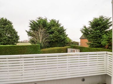 A balcony with white railing overlooking hedges trees and a shed near a house at Lampland House in Walberswick