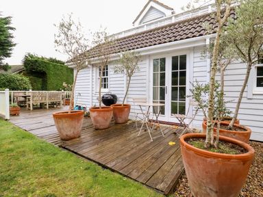 A wooden deck outside a white house with potted trees a small table with two chairs and a dining table with benches at Lampland House in Walberswick