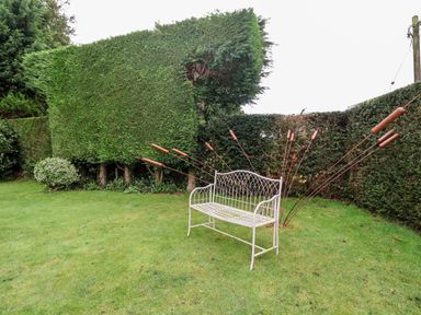 A metal bench on grass with tall hedges and metal garden decorations behind it at Lampland House in Walberswick