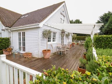 A wooden deck with outdoor furniture and potted plants along the side of a white house at Lampland House in Walberswick