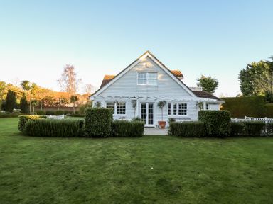 A white house with a gable roof surrounded by grass and shrubs at Lampland House in Walberswick