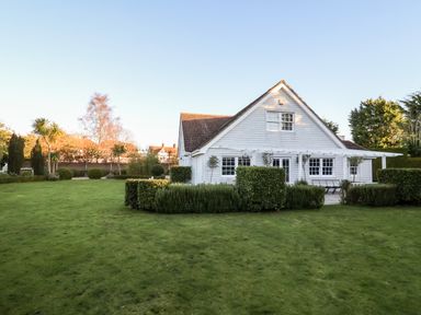 A white house with a sloped roof surrounded by a large green lawn and trimmed bushes at Lampland House in Walberswick