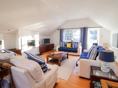 A living room with three sofas a wooden coffee table a television and blue striped curtains at Lampland House in Walberswick