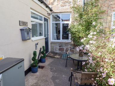 An outdoor patio area with a small table and two chairs with plants and flowers at Seascape Cottage in Seahouses