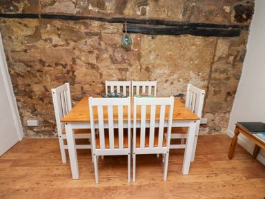A dining area with a wooden table and five white chairs against a stone wall at Seascape Cottage in Seahouses