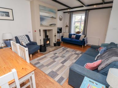 A living room with two blue sofas a blue armchair a wood burning stove and a wooden dining table at Seascape Cottage in Seahouses