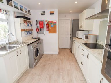 A kitchen with white cabinets a washing machine a dishwasher a refrigerator a microwave and a sink at Seascape Cottage in Seahouses