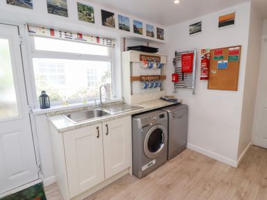 A utility room with a sink washing machine dishwasher and mugs on a rack at Seascape Cottage in Seahouses