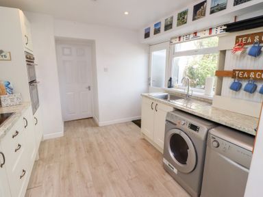 A kitchen with white cabinets a washing machine a dishwasher a sink and a door with pictures above at Seascape Cottage in Seahouses