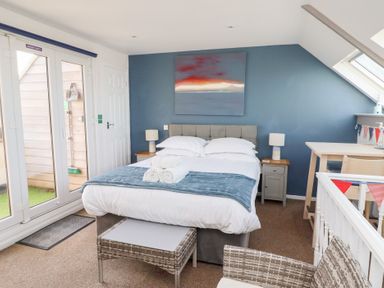 A bedroom with a double bed bedside tables lamps a desk and chair and patio doors at Seascape Cottage in Seahouses
