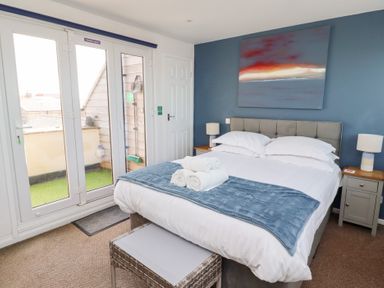 A bedroom with a double bed bedside tables and lamps and a door leading to a balcony at Seascape Cottage in Seahouses