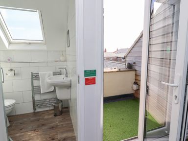 A bathroom with a sink and towel rail next to a balcony with artificial grass at Seascape Cottage in Seahouses
