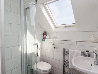 A bathroom with a shower enclosure toilet sink towel rack and skylight window at Seascape Cottage in Seahouses