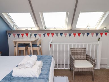 A bedroom with a bed with folded towels a small dining table with chairs and a wicker chair near three skylight windows at Seascape Cottage in Seahouses