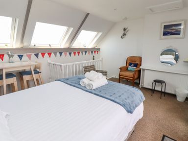 A bedroom with a bed towels on a blanket near windows a table with chairs and an armchair at Seascape Cottage in Seahouses