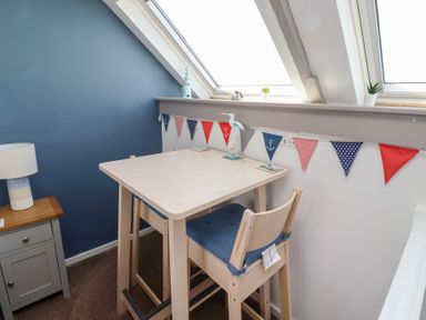 A small dining area with a table and two chairs under skylight windows with nautical bunting and a lamp on a side table at Seascape Cottage in Seahouses