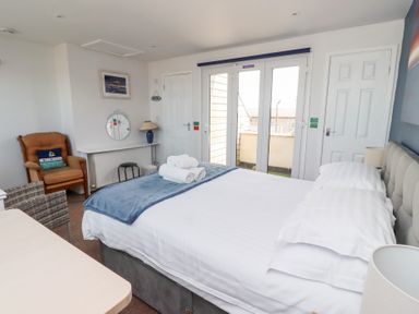 A bedroom with a bed towels on a blanket a chair a desk lamp and double doors leading outside at Seascape Cottage in Seahouses