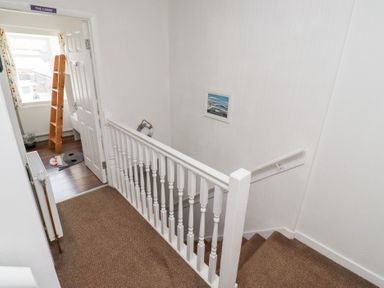 A hallway with brown carpeted stairs and white railing leading to a room with wooden floor and a shark rug at Seascape Cottage in Seahouses