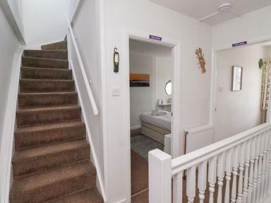 A carpeted stairway next to two doorways with signs above them inside a hallway at Seascape Cottage in Seahouses