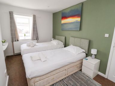 A bedroom with two single beds side by side bedside table and window with curtains at Seascape Cottage in Seahouses