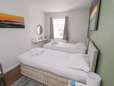 A bedroom with two single beds and a window with curtains at Seascape Cottage in Seahouses