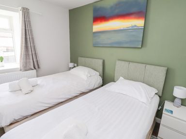 A bedroom with two single beds bedside tables lamps a window and a painting on the wall at Seascape Cottage in Seahouses