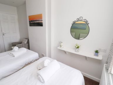 A bedroom with two single beds with rolled towels a wall mirror a small shelf with plants and a chair in the corner at Seascape Cottage in Seahouses