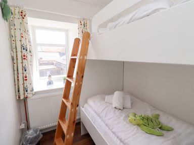 A small bedroom with a bunk bed wooden ladder and a window with patterned curtains at Seascape Cottage in Seahouses