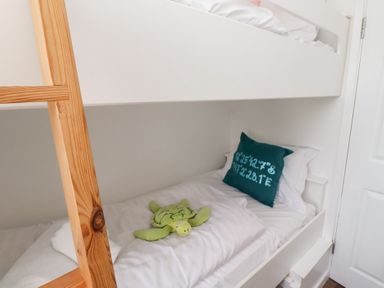 A bunk bed with a wooden ladder a lower bed with white bedding a green turtle toy and a dark green pillow with coordinates at Seascape Cottage in Seahouses