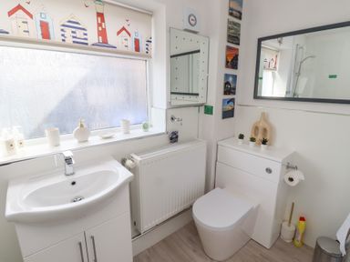 A bathroom with a sink cabinet a toilet a radiator and decorative items on the windowsill at Seascape Cottage in Seahouses