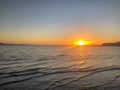 A sunset over the ocean with small waves and a distant shoreline at Brewers Quay Harbour