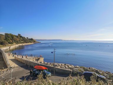 A coastal walkway with people standing near the water kayaks on a car roof and calm sea at Melanie's Cottage in Brewers Quay Harbour
