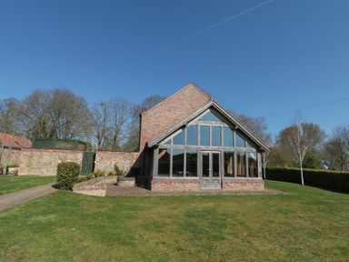 A brick building with large glass windows and a pitched roof in a grassy yard with trees at The Barn Helperby near Boroughbridge