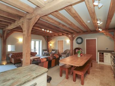 A living room and kitchen area with wooden beams on the ceiling and a dining table with benches at The Barn Helperby near Boroughbridge