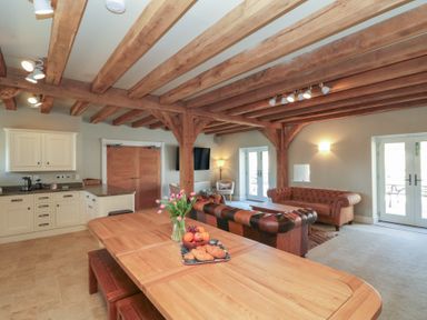 A living room with wooden beams ceiling a wooden table with flowers and croissants a leather sofa and armchair at The Barn Helperby near Boroughbridge