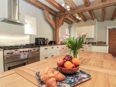 A kitchen with wooden beams on the ceiling a stove a wooden table with croissants fruit bowl and flowers at The Barn Helperby near Boroughbridge