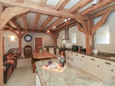 A kitchen with wooden beams cabinets and a dining table with flowers at The Barn in Helperby near Boroughbridge