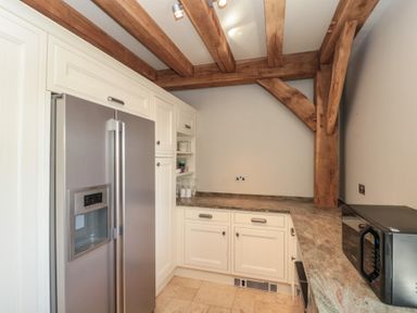 A kitchen with stainless steel refrigerator white cabinets wooden ceiling beams and a microwave on the counter at The Barn Helperby near Boroughbridge