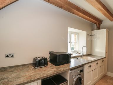 A kitchen counter with toaster microwave sink washing machine and wooden ceiling beams at The Barn Helperby near Boroughbridge