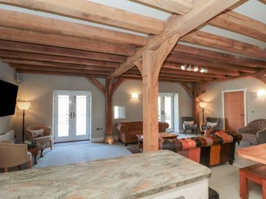 A living room with exposed wooden beams leather sofas chairs and double doors at The Barn Helperby near Boroughbridge
