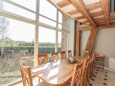 A dining room with wooden table and chairs near large windows showing a garden at The Barn in Helperby near Boroughbridge