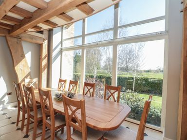 A dining room with a wooden table and chairs next to large windows showing a garden at The Barn in Helperby near Boroughbridge
